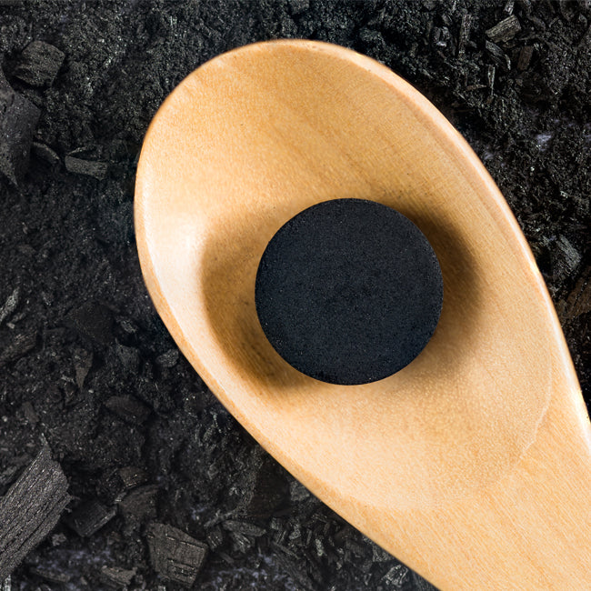 image showing a pile of active carbon pieces as a background with a wooden spoon and one piece of carbon lying on it.