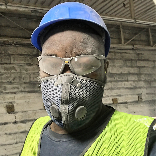 man on a jobsite wearing an rz mask m2 to protect against dust and other particulates. He is also wearing a hardhat, a yellow vest and safety glasses