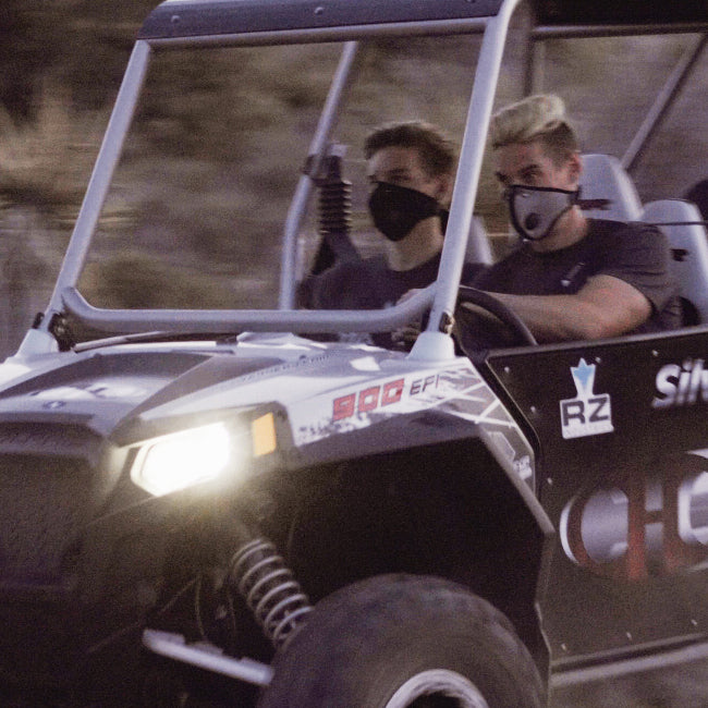 two men in a UTV wearing RZ Mask M2 Titanium masks to protect from dust while on their ride.