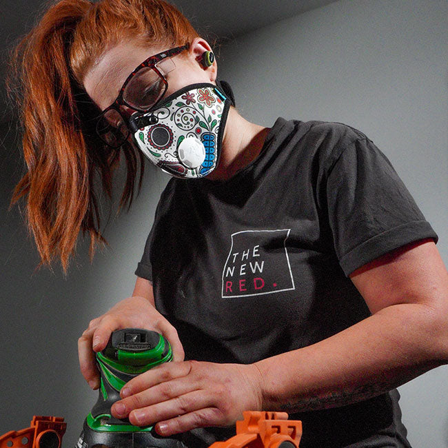 woman with red hair wearing rz mask m2n day of the dead shell while using a palm sander