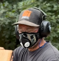 Man wearing a camo respirator mask and earmuff hearing protection while working outdoors.
