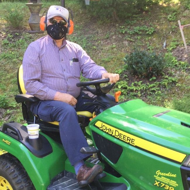 Man on a John Deere lawn mower wearing an RZ Mask M1 Neoprene Black mask to protect from pollen and dust while mowing.