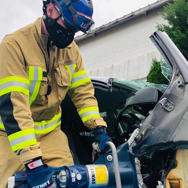 Firefighter wearing an rz mask m1 black to protect from particulates while using a saw on a car door.