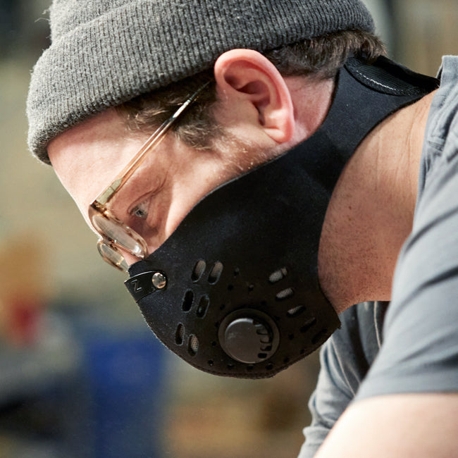 Man wearing an rz mask m1 black neoprene mask with a beanie hat and glasses in a workshop for dust protection
