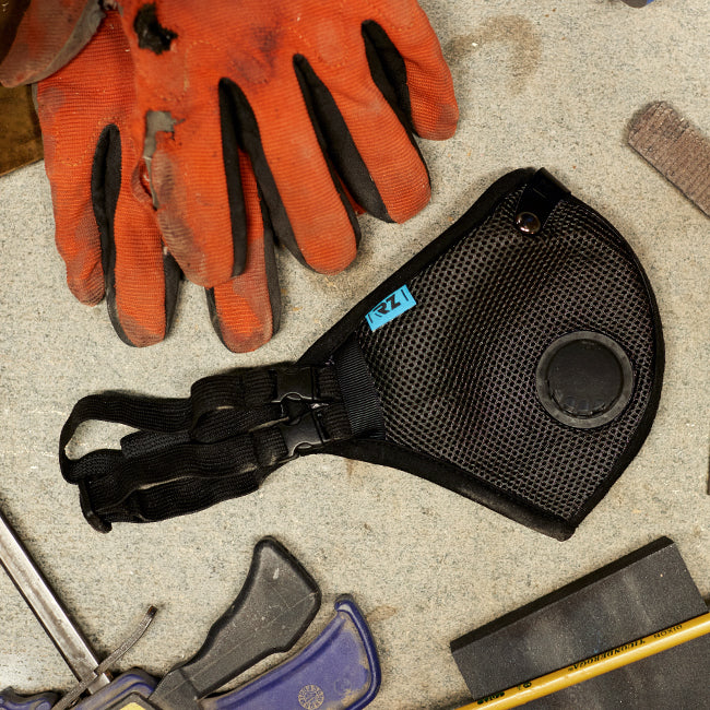 An rz mask m2.5 black laying on a table with some sawdust, a pair of gloves and some other tools