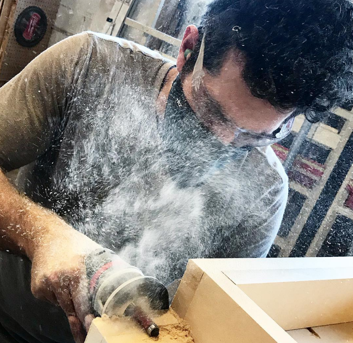 Man wearing an rz mask M2 black mask while using a router tool in a wood shop for protection from the large amount of dust flying in the air.