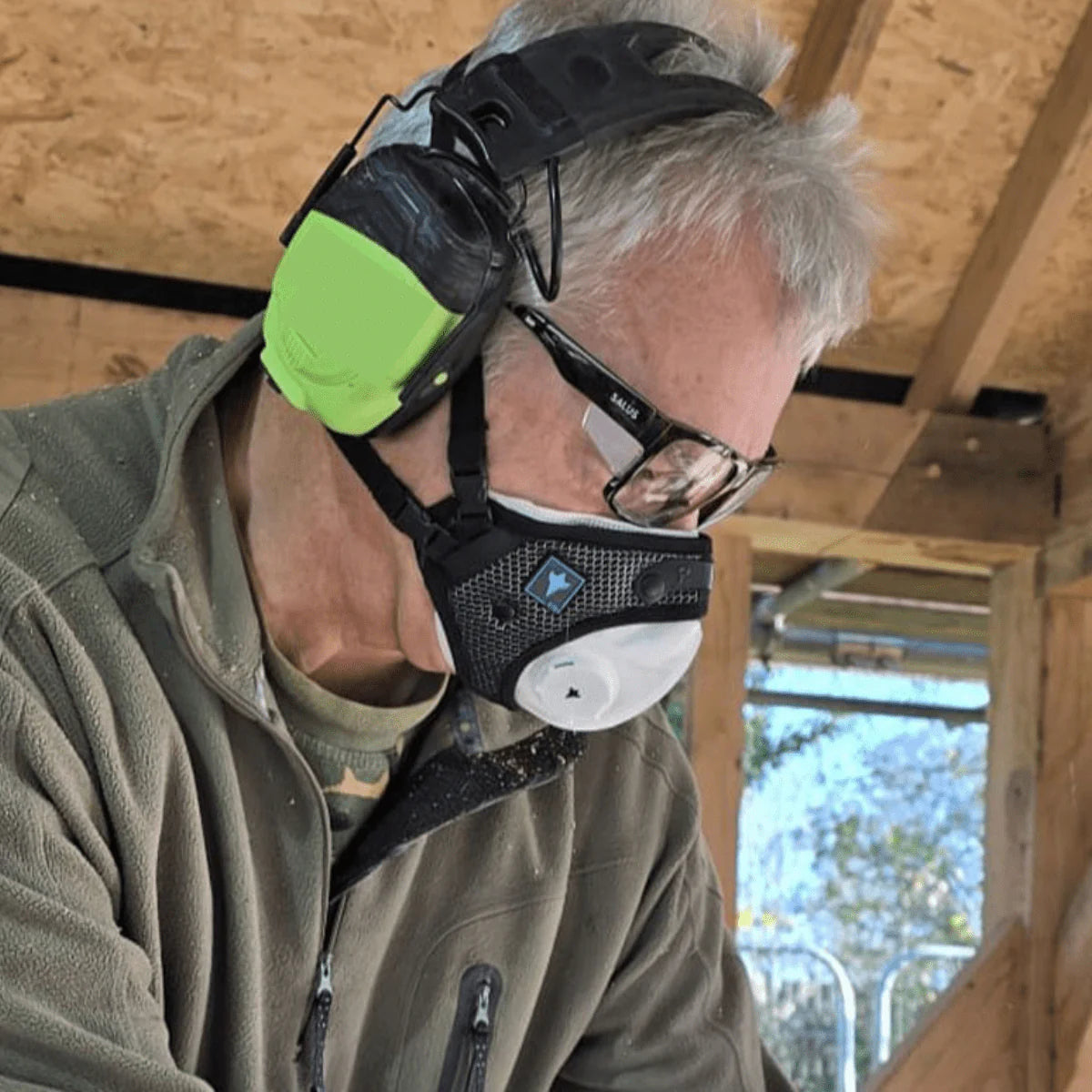 Person wearing a black and green glove with a white face mask indoors.