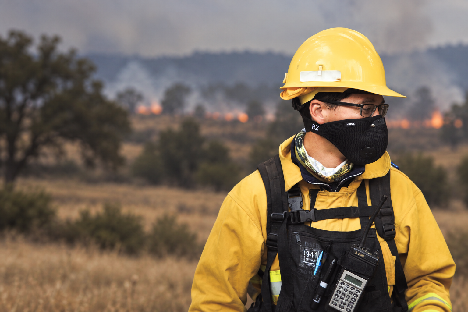 Firefighter with a softly blurred field and distant grass fire behind him